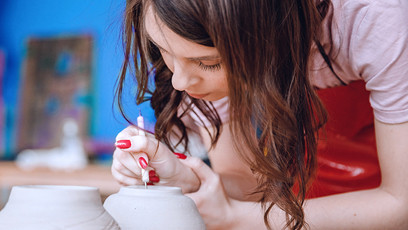 A businesswoman looking down and carefully etching something into a piece of pottery.