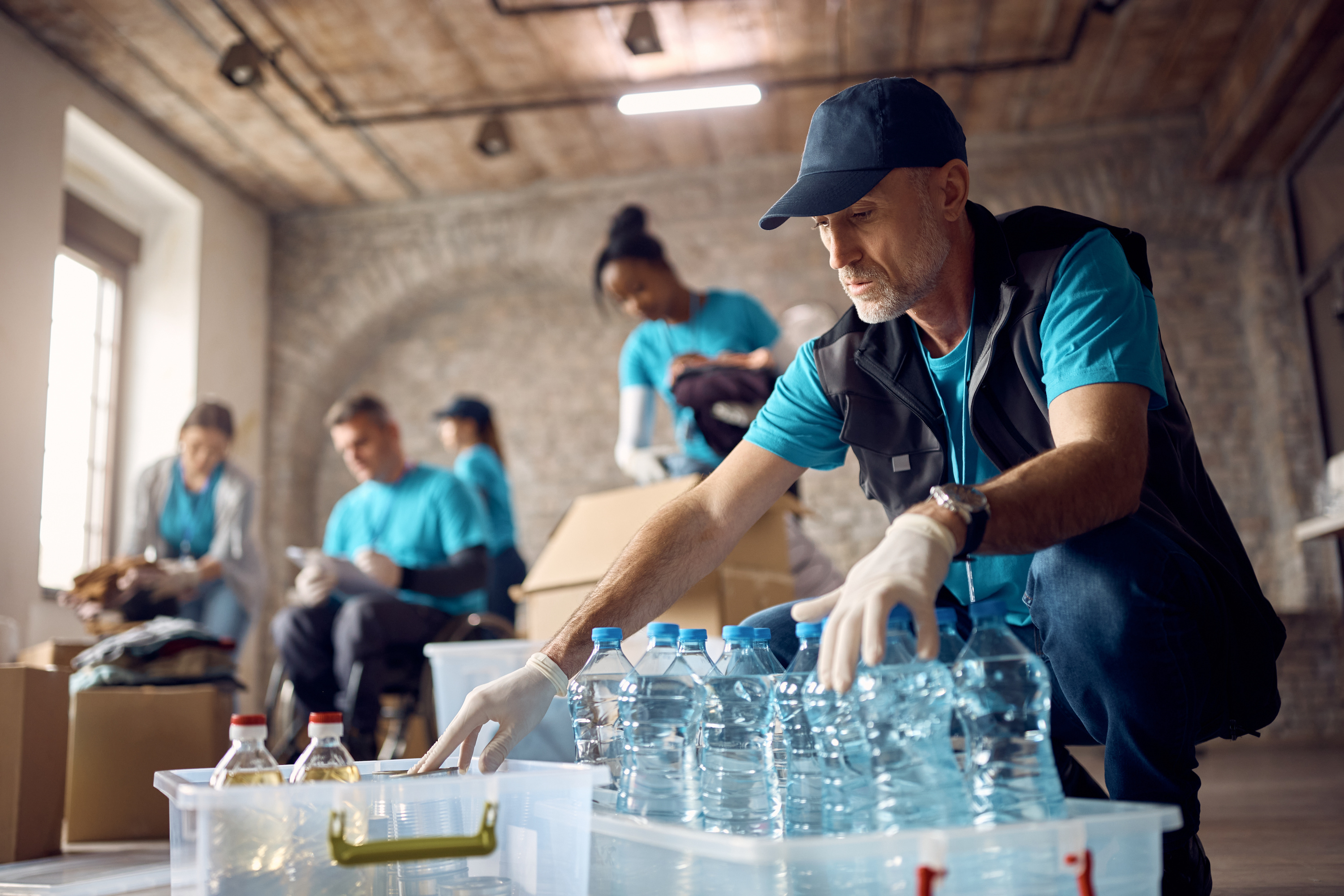 A man in a vest, hat, and gloves, puts bottled drinks into a plastic tub. The warehouse where he works has a DBA that's different than the name of the LLC.