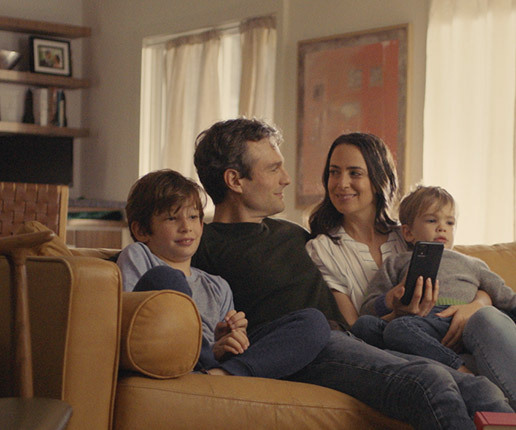 Mom and dad smiling on the couch with their kids as they create their estate plan on a smartphone