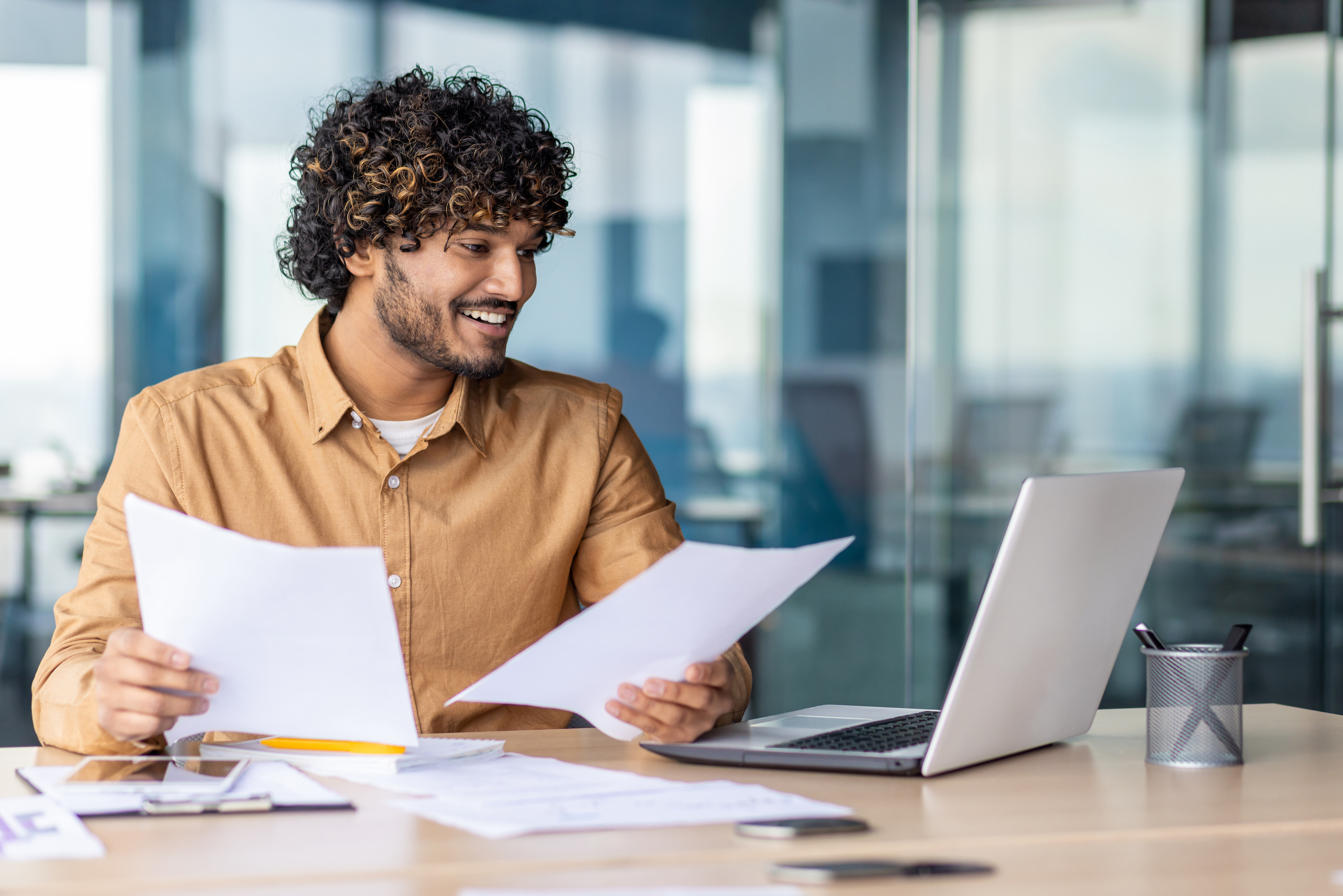 A man seated at a desk with papers in his hands looks at his open laptop as he completes his formation documents for his new LLC.