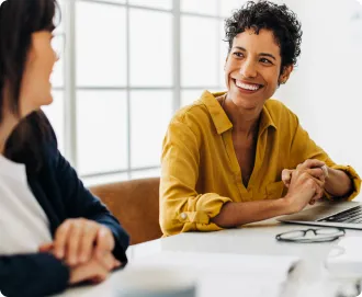 Latina with short curly hair wearing a mustard yellow shirt sitting at her desk with her laptop talking to colleagues about how to grow their business with LegalZoom partners.