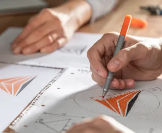 White man's hands holding an orange and silver pen working on a drafting project after registering his trademark with LegalZoom.