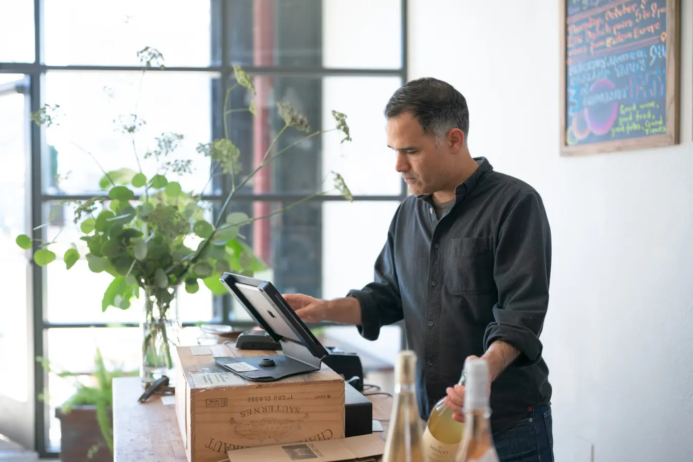 A man standing in front of the point of sale system at a wine store that has recently filed for a DBA.