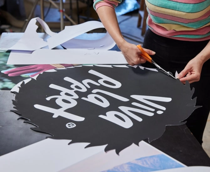 Artist from Viva la Puppet wearing a multicolored striped shirt cutting out the Viva la Puppet logo after their trademark was registered with LegalZoom.