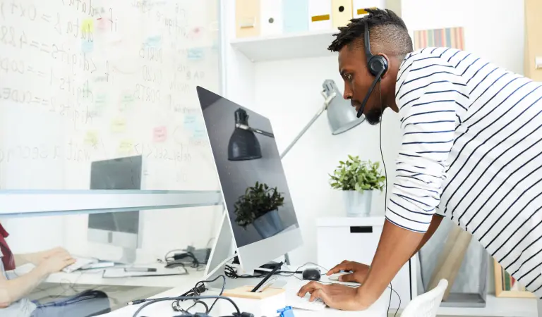 Black man wearing a black and white striped shirt. Wearing a headset and standing in front of his desktop in his home office after incorporating his business with LegalZoom.